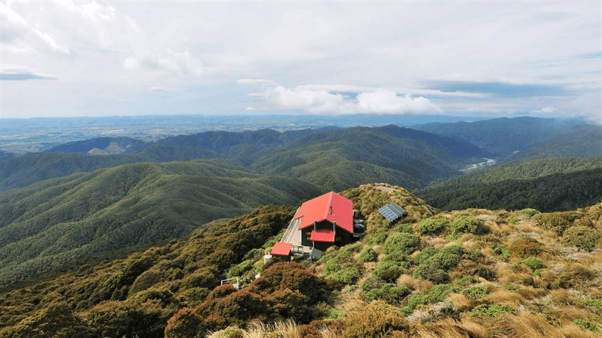  backcountry hut with a red roof on a mountain ridge, overlooking a mountainous terrain