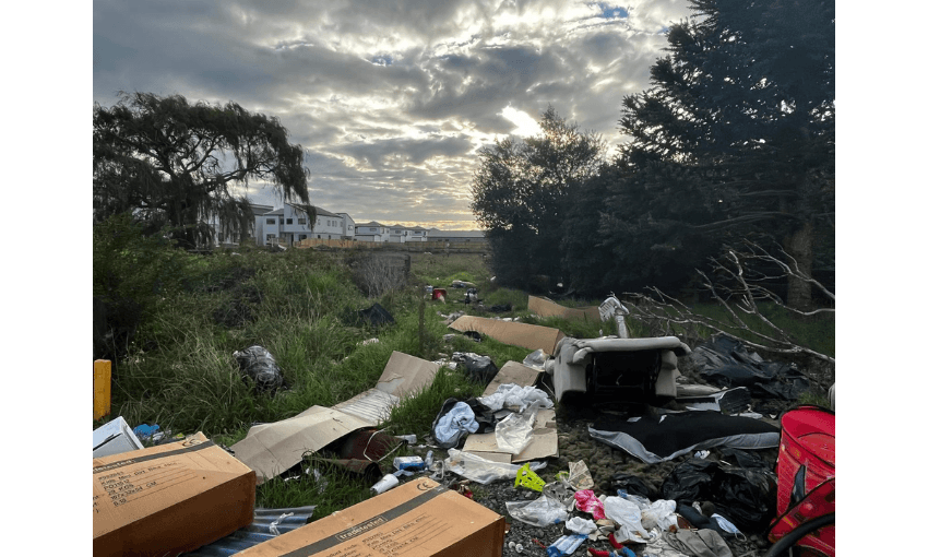 Photograph showing a new development of residential housing with a trail of destruction and debris behind it. Bright sun is behind clouds.