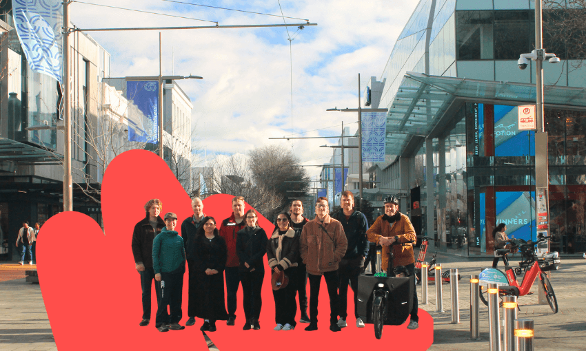 a group of people standing on a christchurch street with a red squiggle behind them. several have bikes; all are smiling but look a bit cold.