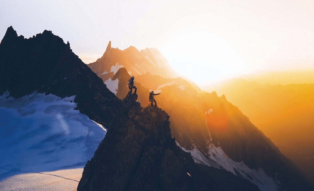 two people on mountain ridge as sun sets