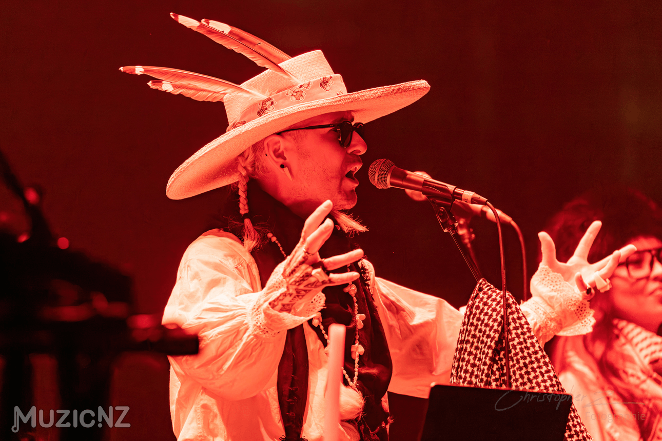 photo of person singing in a wide brimmer hat with feathers pointing out