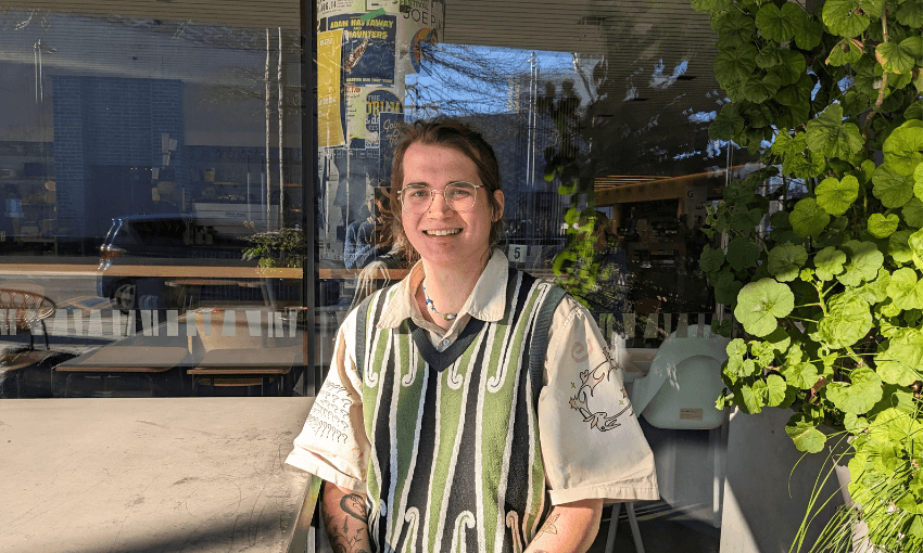 a person sitting in the sunshine at a table in a green and black vest with a white button up shirt underneath smiling
