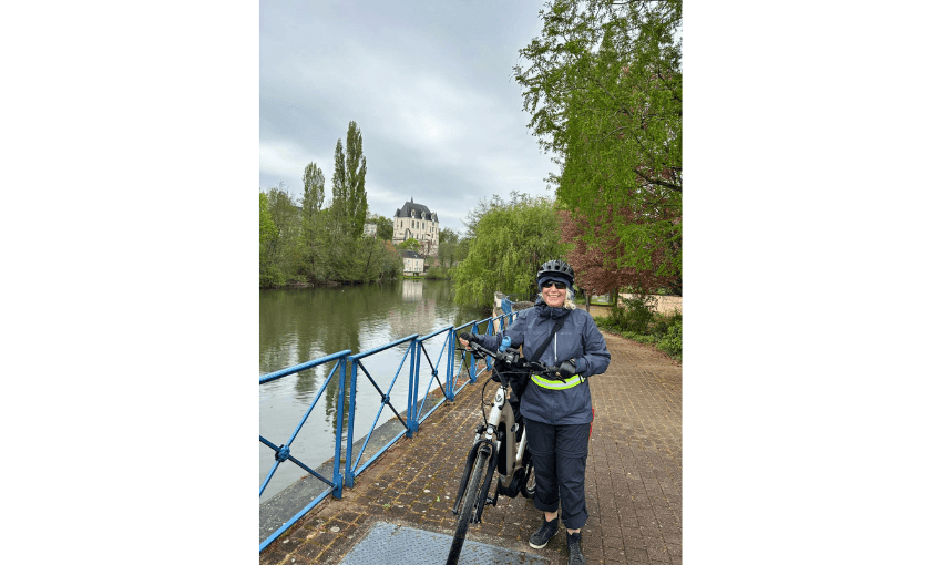 Photograph of Maria Gill with her bike, with canal beside her and French chateau in background.