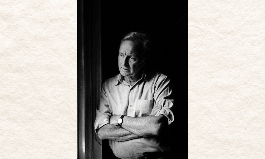 A man is standing leaning against a wall, looking off to the right. He has his arms crossed. The photo is in black and white.