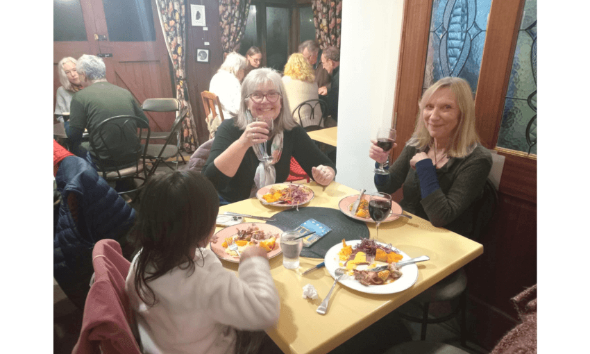 A dinner table set with kai and red wine. Two women hold up their glasses in cheers. A small child is sitting at the table with them. 