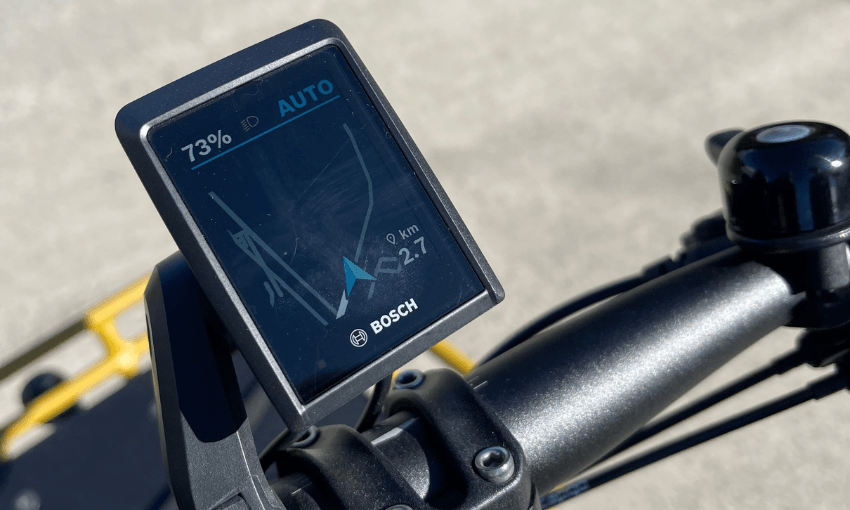 Close-up of a Bosch e-bike smart system display showing a map, route directions, 73% battery, and "AUTO" mode, mounted on the handlebars against a blurred outdoor background.