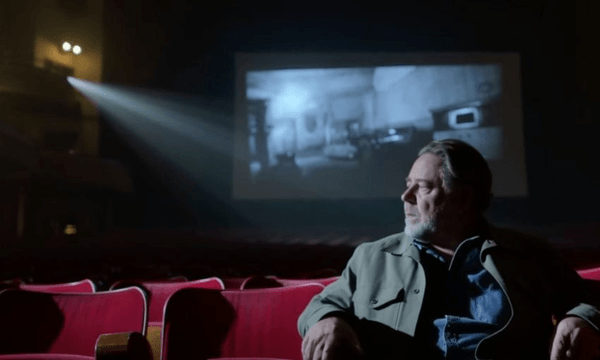 A screenshot from the Hollywood Avondale PS, showing AI Russell Crowe sat on cinema seats which are positioned with the movie screen behind them.