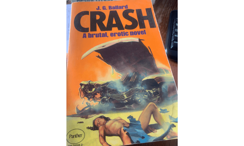 The cover of JG Ballard's novel CRASH which is orange with a drawing of a busted car and a woman lying on the ground covered in debris.