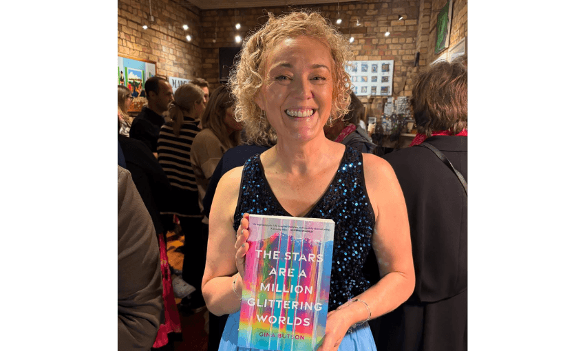 Photograph of a woman holding up her book in a crowded room and smiling.