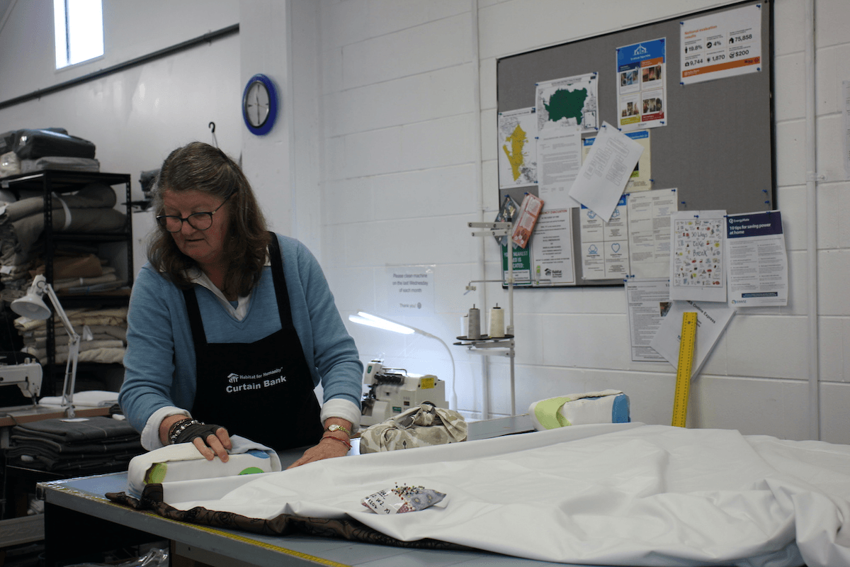 woman at a pattern cutting table in a sewing room wearing an apron