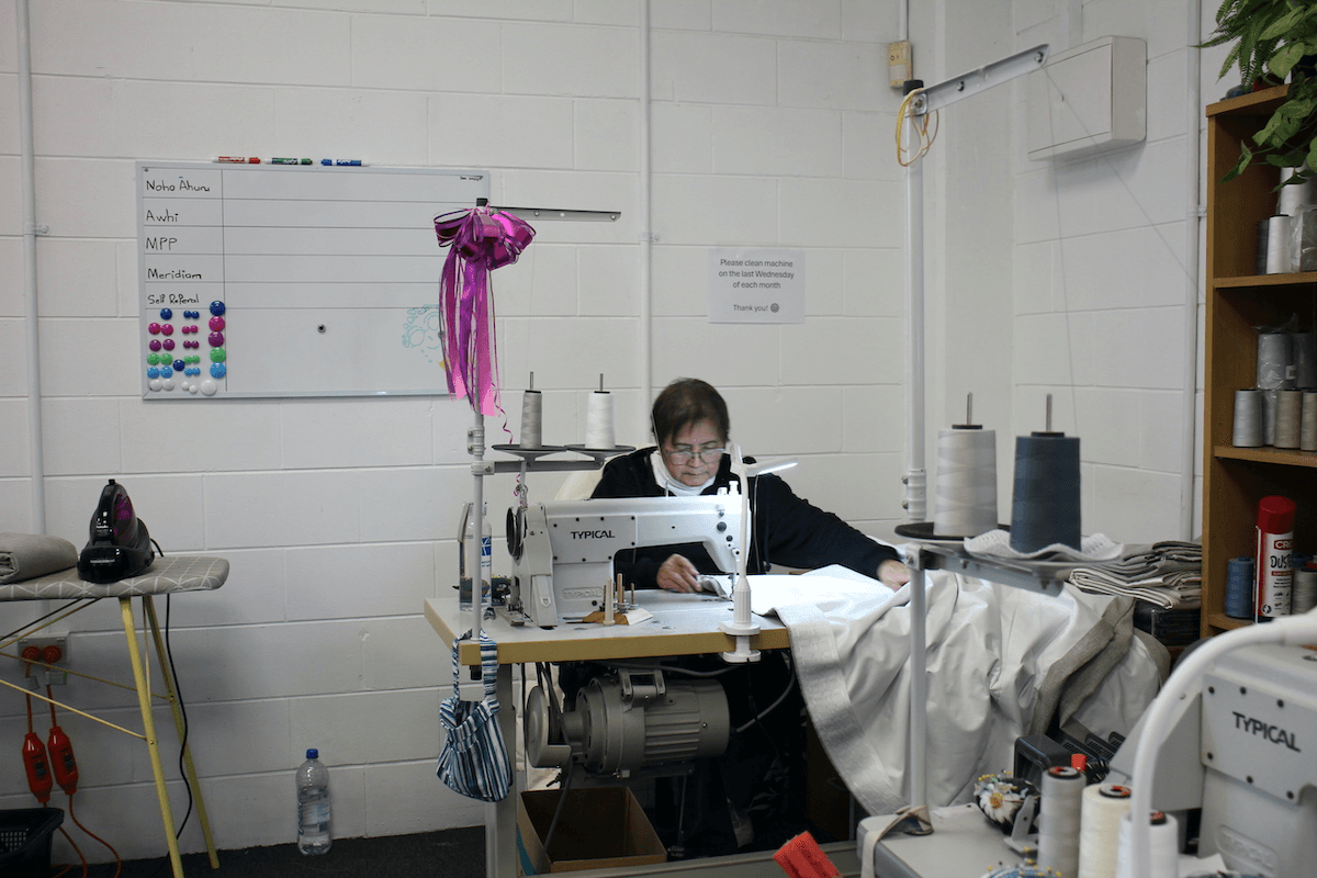 woman sitting at an industrial sewing machine, guiding a curtain through.