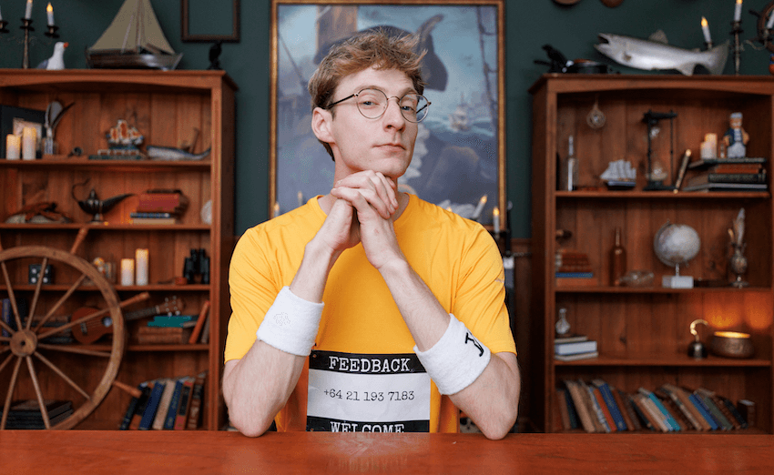 Jack Ansett raises one eyebrow to the camera, wearing a yellow tshirt with his phone number on it