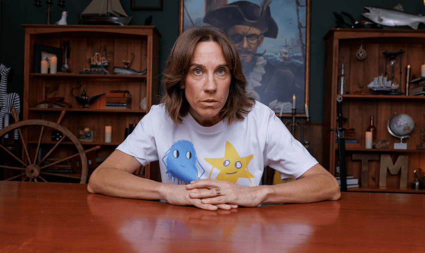 Jackie wears a white tshirt and stares down the camera in front of assorted naval objects