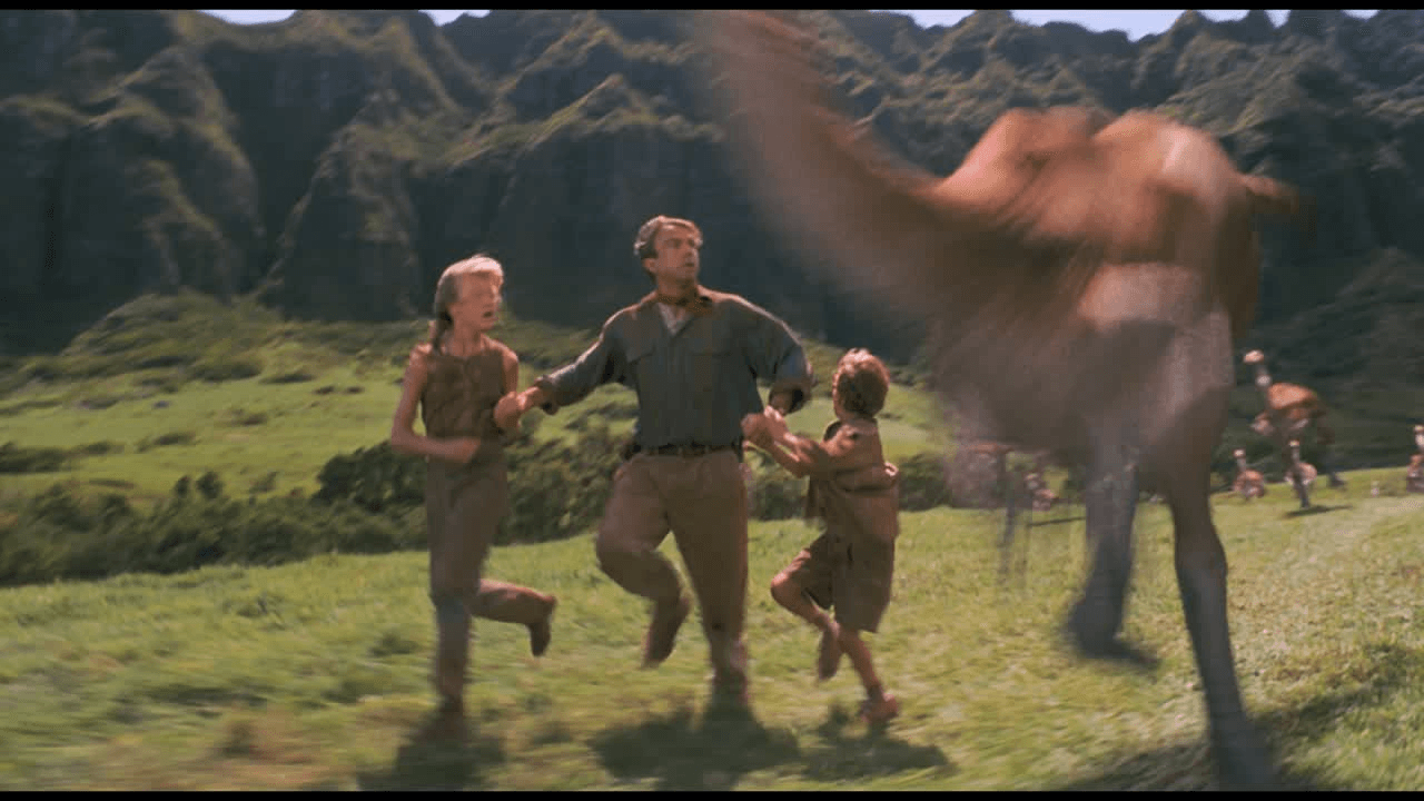 A film still of three humans running from dinosaurs.