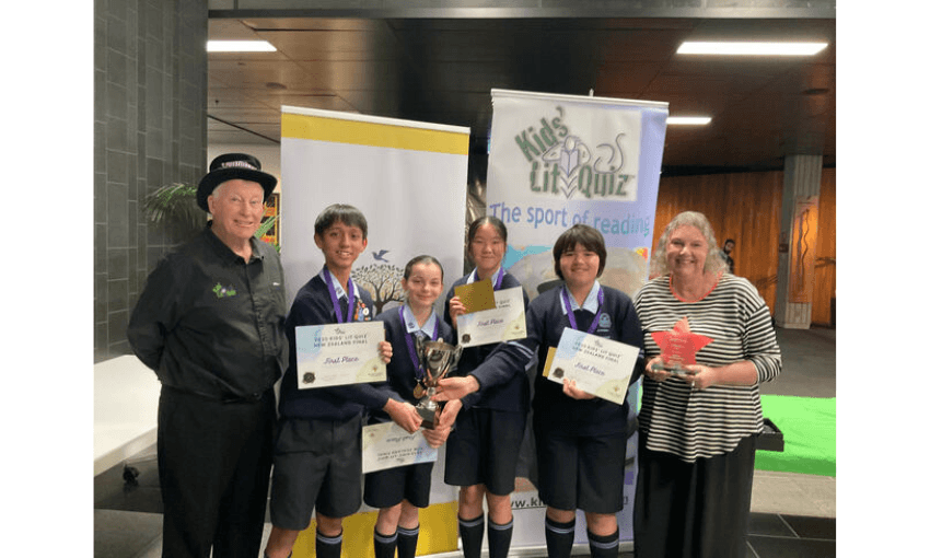 A man with a top hat is on the left, four children aged approximately 11 years old beside him in a row holding certificates, and a woman on the right smiling.