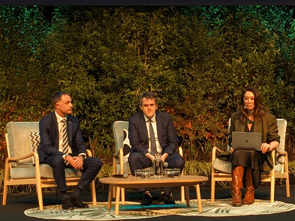 two men and mirama kamo on a stage with foliage behind