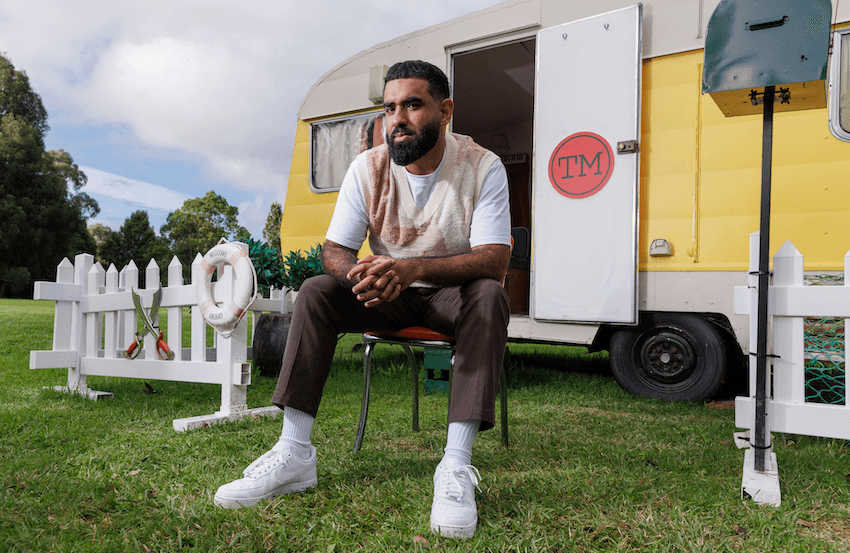 Pax Assadi sits on a chair in front of the Taskmaster caravan
