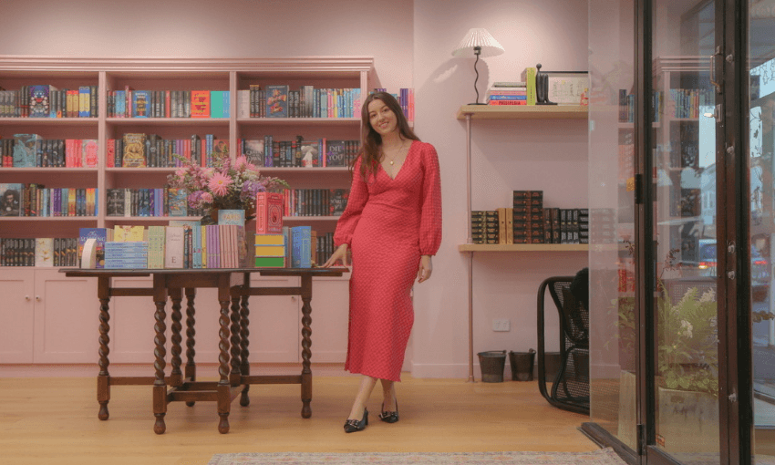 A woman in a red dress is standing in a bookshop. She is smiling. 