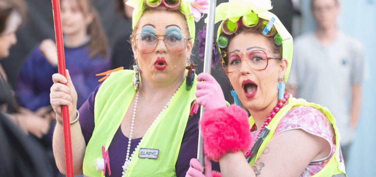 two ladies dress up wearing a lot of colourful make up hair rollers and high-vis vests