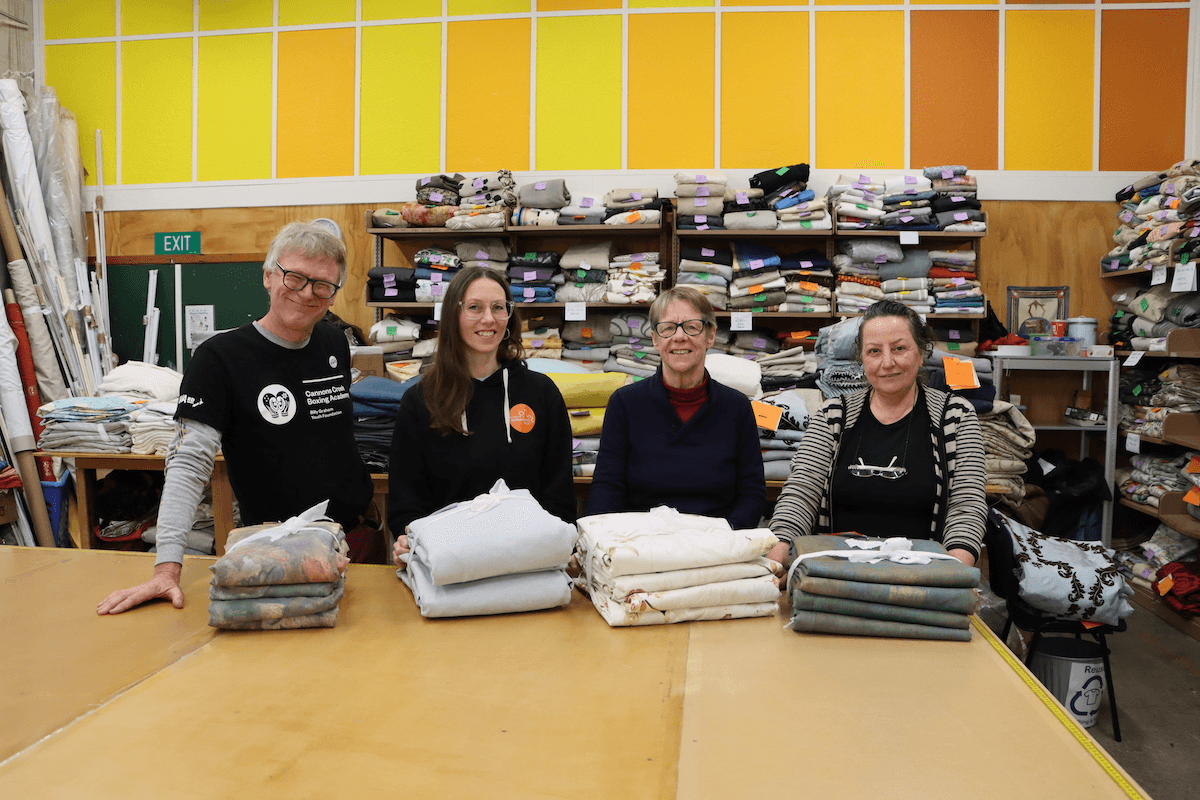 four people smiling standing in front of a pattern cutting table with budnles of curtains. behind them are shevles full of curtains