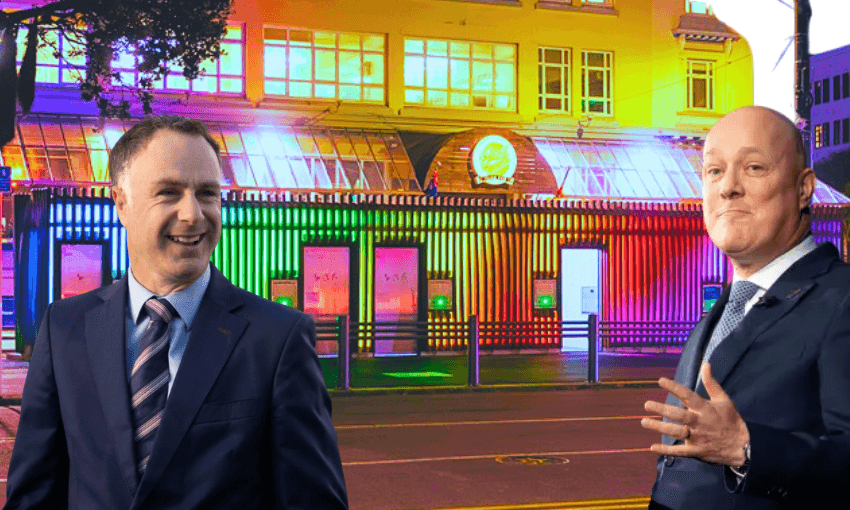 Two men in suits in front of a colourfully-lit building