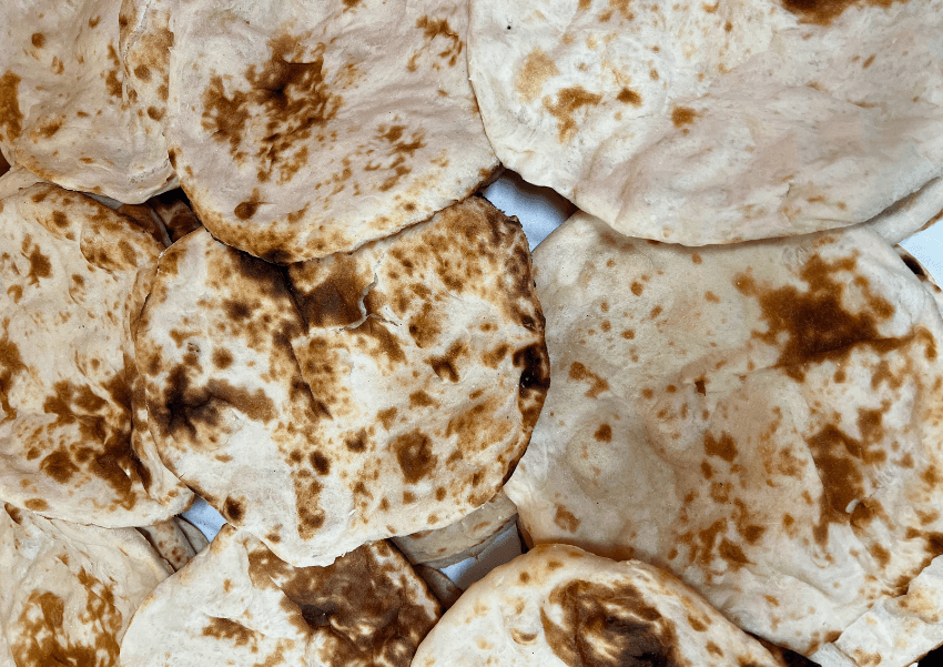 Several pieces of flatbread with golden brown, slightly charred spots are stacked closely together, showing their round shapes and soft, textured surfaces.