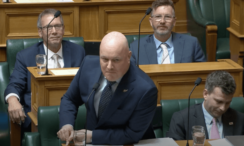 Christopher Luxon stands in the House with his finger pointed firmly on his bench.