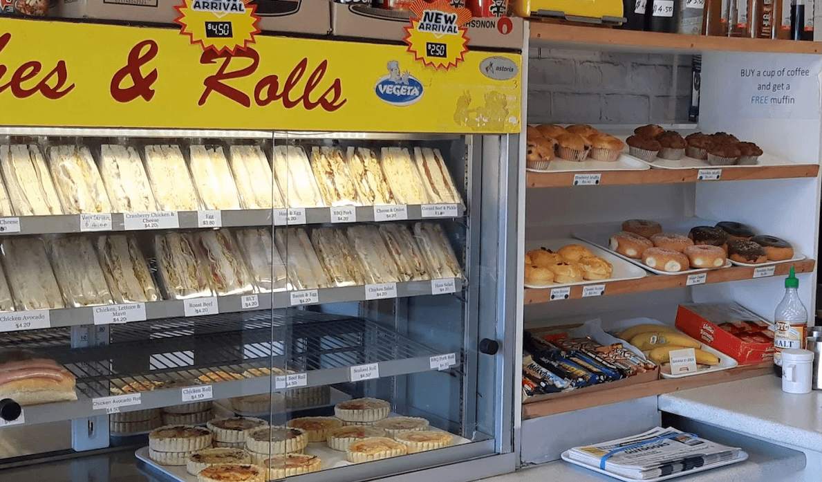 rows of club sandwiches next to some sweet goods and chocolate bars inside a bakery