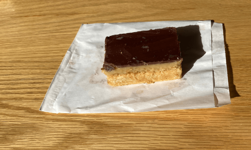 a chocolate caramel slice on a white paper bag on a wooden table