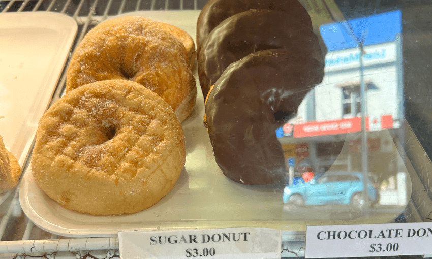 a tray of sugar donuts and chocolate donuts behind a glass