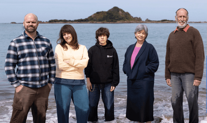 five people standing on the shore with an island behind them