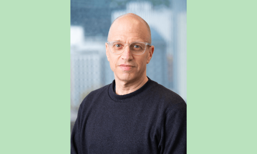 a green backgroun, a bald man with glasses and pale skin looking at the camera with a serious expression