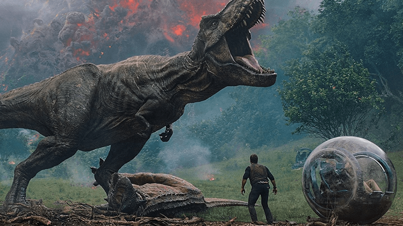 A still from Jurassic World: Fallen Kingdom showing a large T-Rex dinosaur roaring while a man stands beneath it