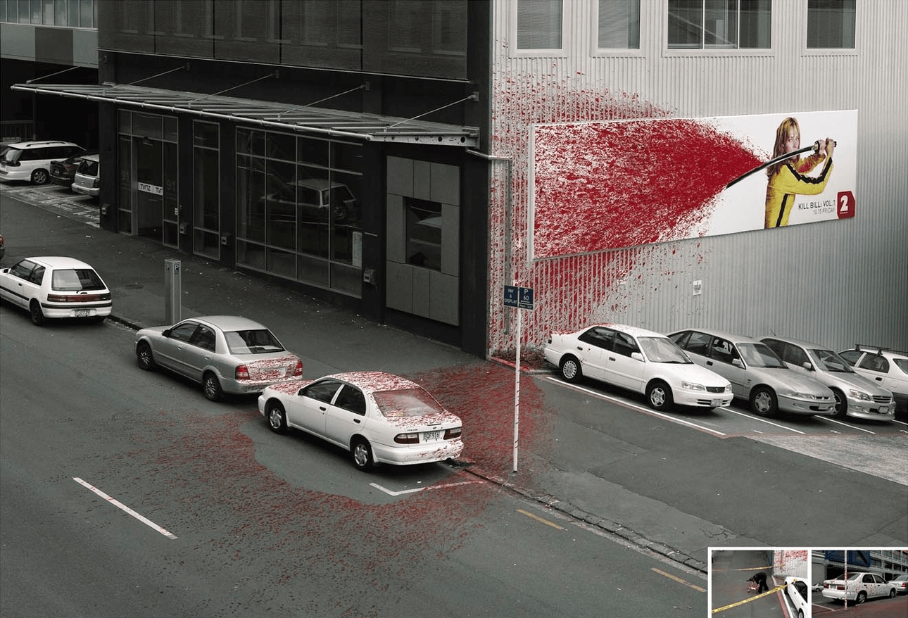 A billboard for the movie Kill Bill on the side of a building. Fake blook is spraying across the billboard and onto a car parked nearby
