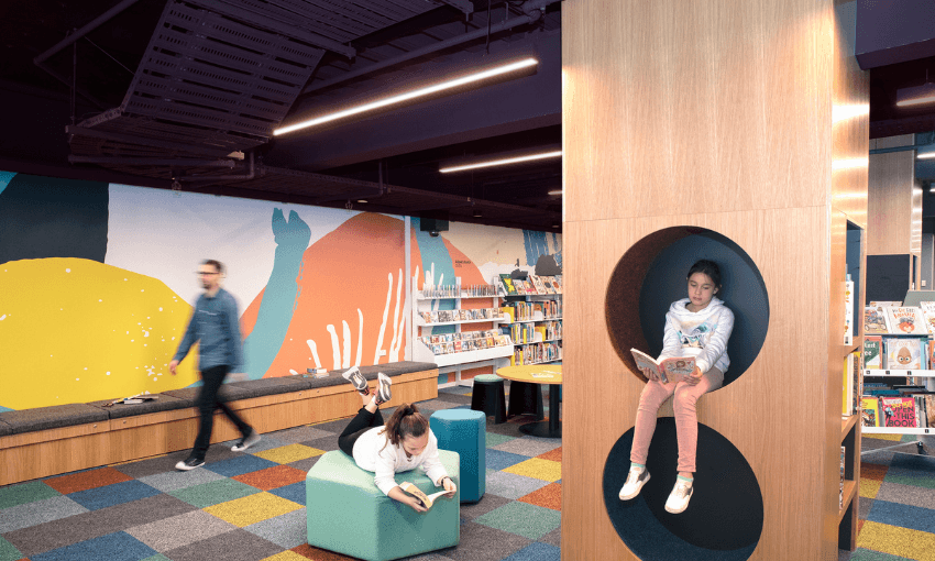 a young girl reading in a nook with colourful carpet and bookshelves behind her and lots of floor space