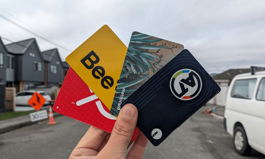a hand holding a snapper card, a Bee card, ametro card and an AT HOP card, with a grey street in the background