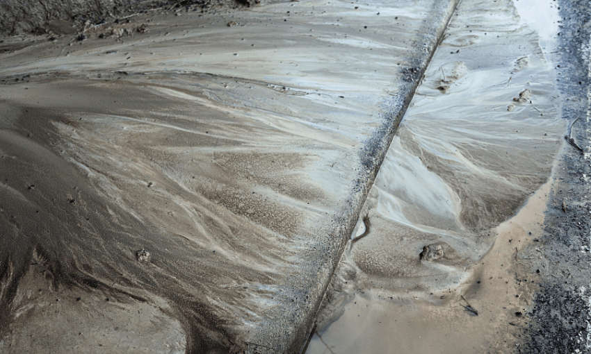 textured brown silt tipping into a drain 