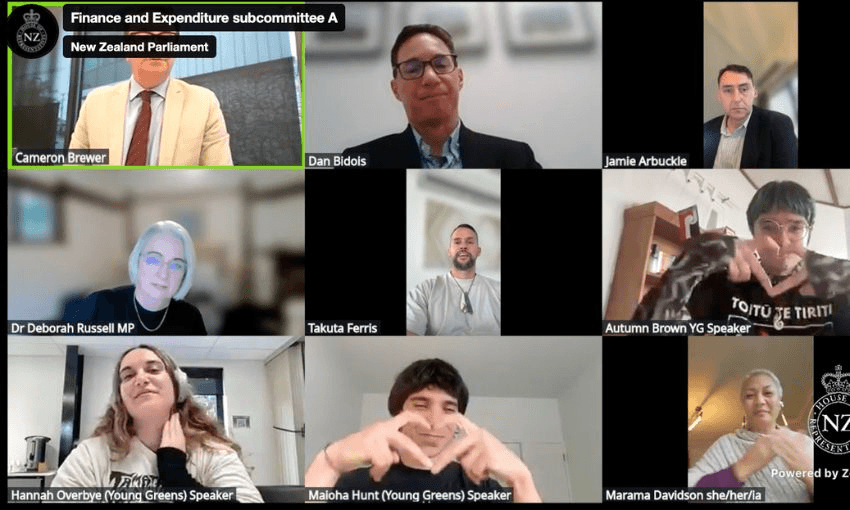 A screenshot from the livestream of the RSB hearings, showing two Young Greens members making heart-hand signs for Marama Davidson, also on screen.