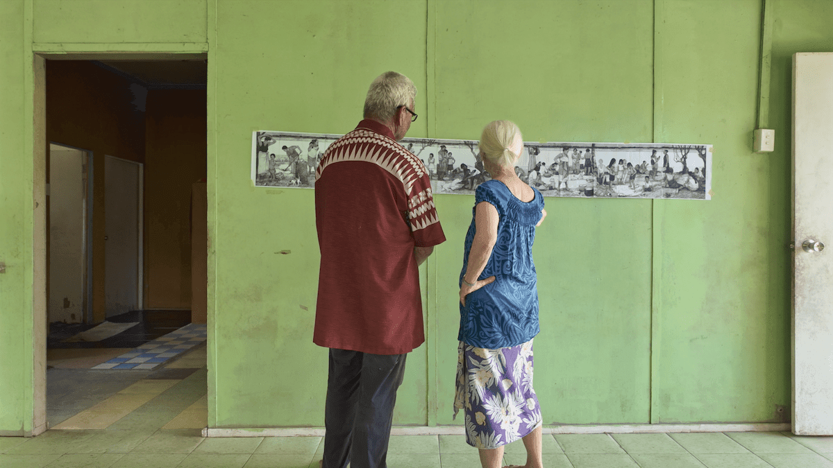 two people look at a very wide printed out picture pinned to a green wall