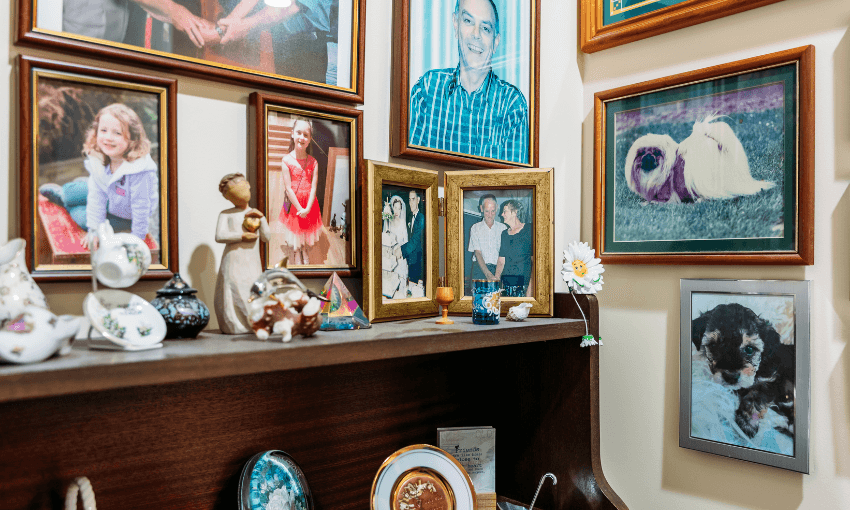 A wooden shelf with decorative items sits below a wall filled with framed family photos, including children, adults, and pets, creating a cozy, personal display.