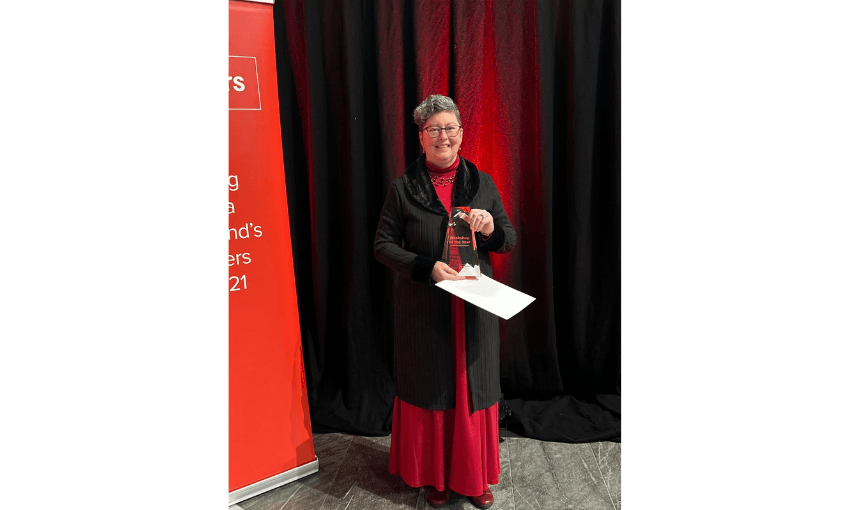 A photograph of a woman wearing a read dress and smiling, holding a trophy.