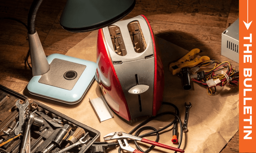 A red and silver toaster is disassembled on a workbench surrounded by tools, wires, a lamp, and a toolkit, with an orange sidebar on the right labeled "THE BULLETIN.