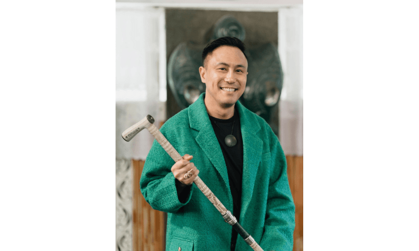 A photograph of Chris Tse holding his Tokotoko. He is wearing a green suit.