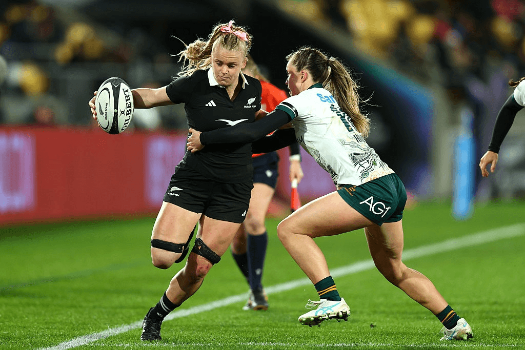 A rugby player in a white uniform attempts to tackle Jorja Miller in black as she runs towards the try line at Wellington Stadium