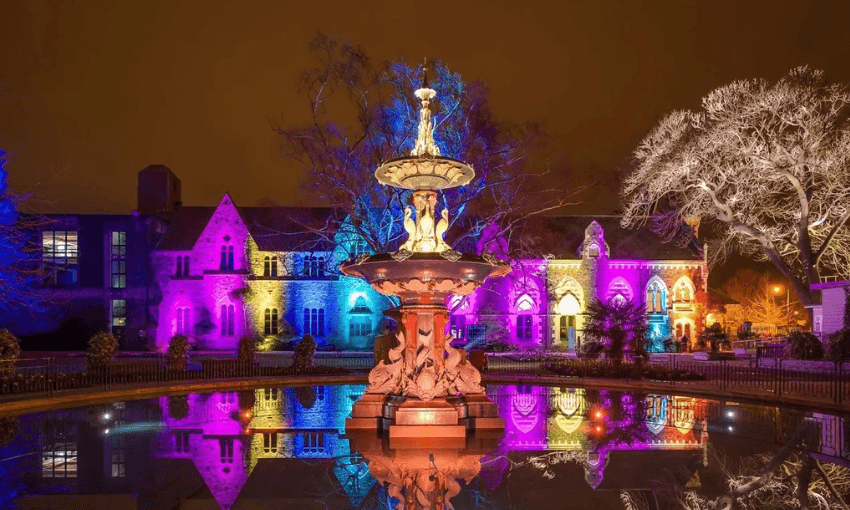 A photograph of a fountain lit up by multi coloured lights.
