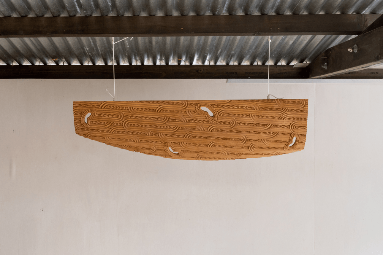 A large, cloud-shaped wooden sculpture — part of Leon Kipa’s Kapua series — hangs from the ceiling of his studio. Carved patterns run across its length, suspended against a plain white wall.