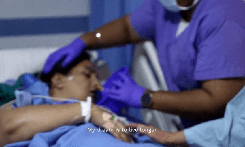 A patient lies in a hospital bed, eyes closed, while a healthcare worker in purple scrubs and gloves cares for them. The scene is emotional, with the text, "My dream is to live longer," overlaid at the bottom.