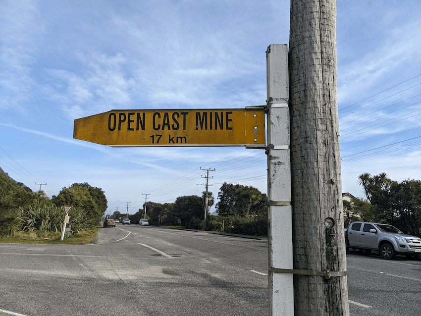 a blue sky and a yellow sign saying 'open cast mine 17 kilometres'