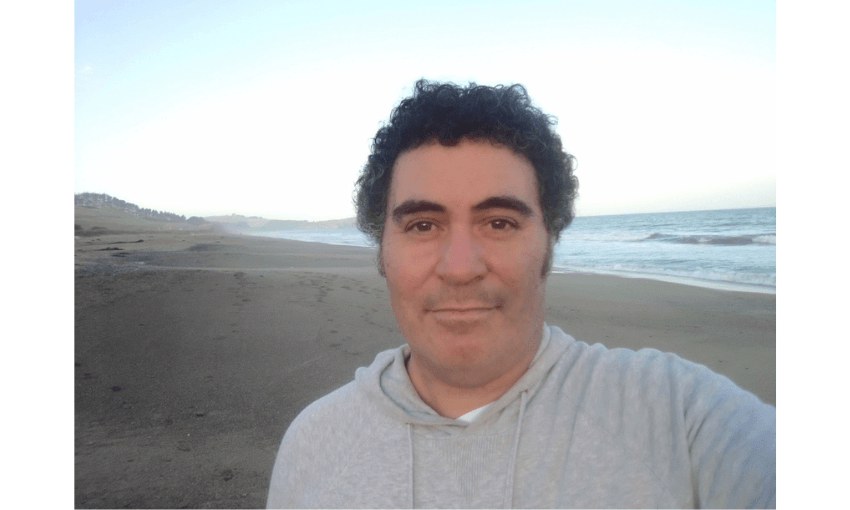 A photograph of a man standing on a beach. 
