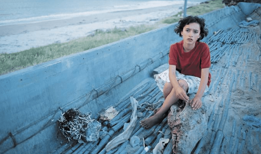 Keisha Castle-Hughes sits on a log near the beach in the 2002 film Whale Rider